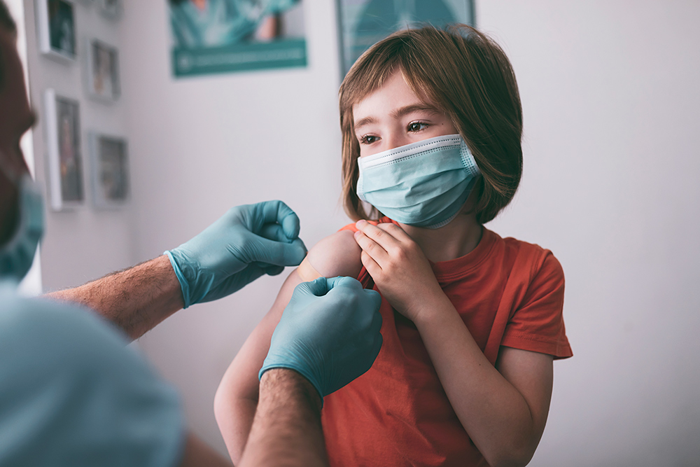 Image of a child wearing a protective face mask, about five years old, getting the Covid-19 vaccine.